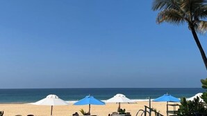 A beach with white and blue umbrellas, a palm tree, and a clear blue sky. - Pearl Island Beach Hotel (Hikkaduwa)