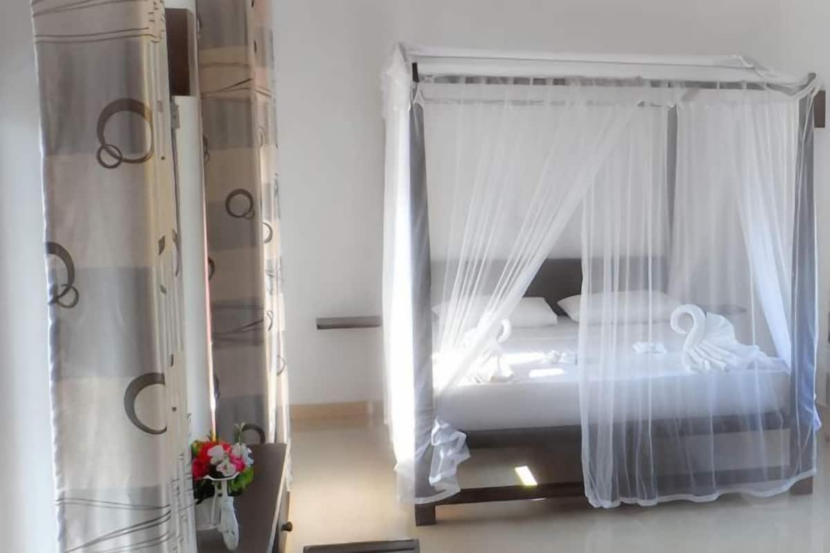 Een bed met hemel, een nachtkastje met een bloevas, en een muur met een cirkelmotief.