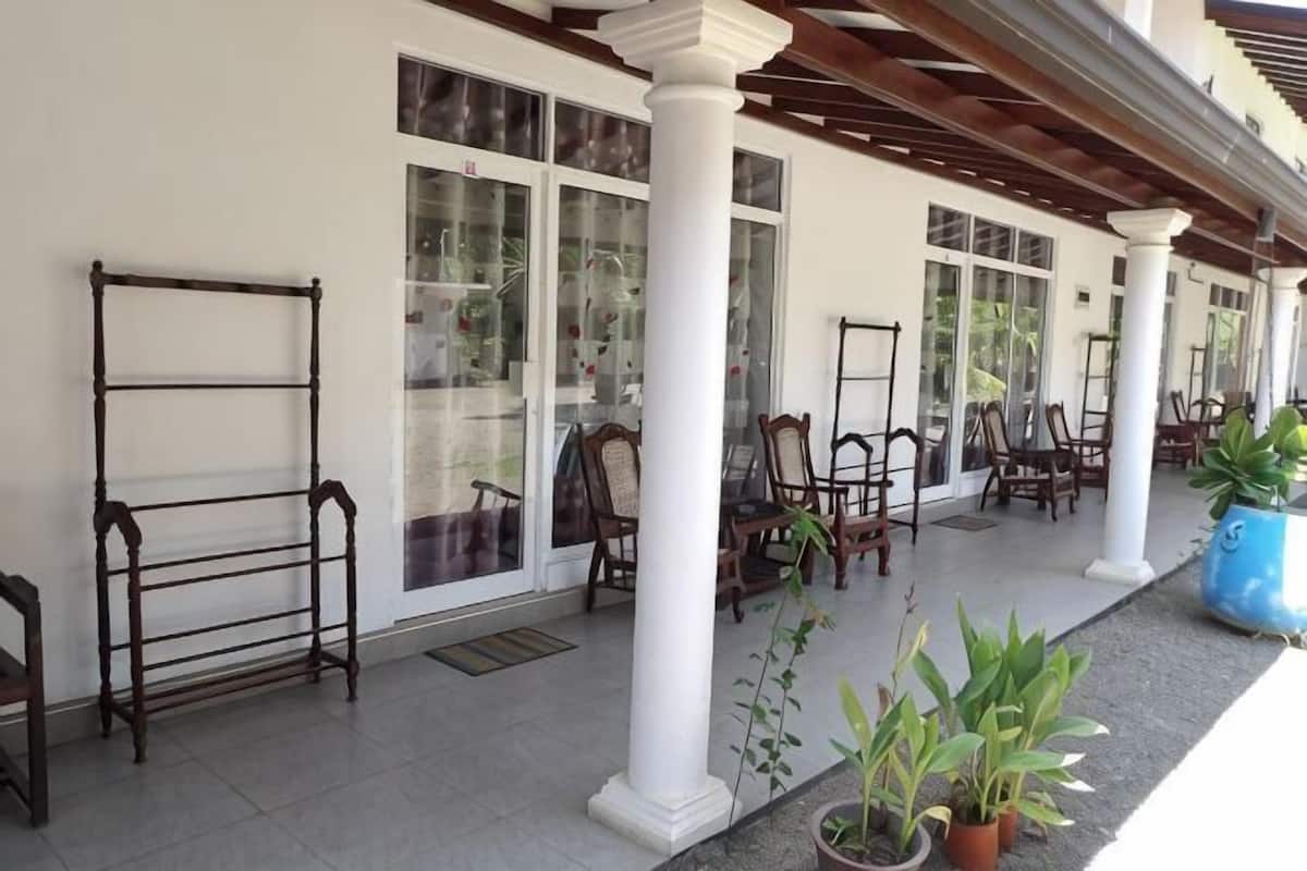 Een overdekt terras met stoelen en tafels, witte zuilen en potplanten.