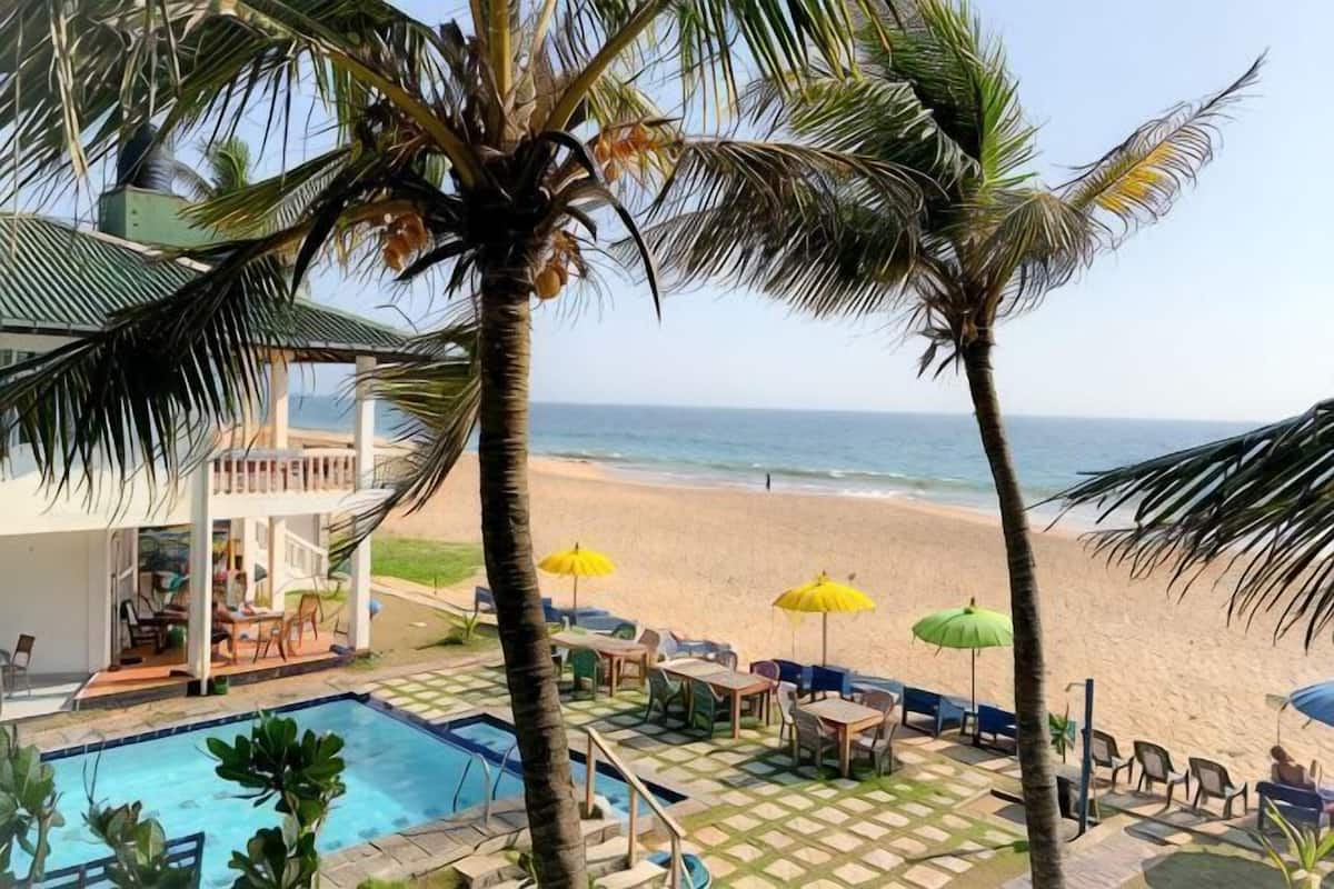 Zwembad met uitzicht op het strand, palmbomen en terrasmeubilair.