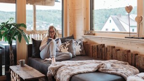 A cozy room with a large window, a sofa, a reading area, and a plant.