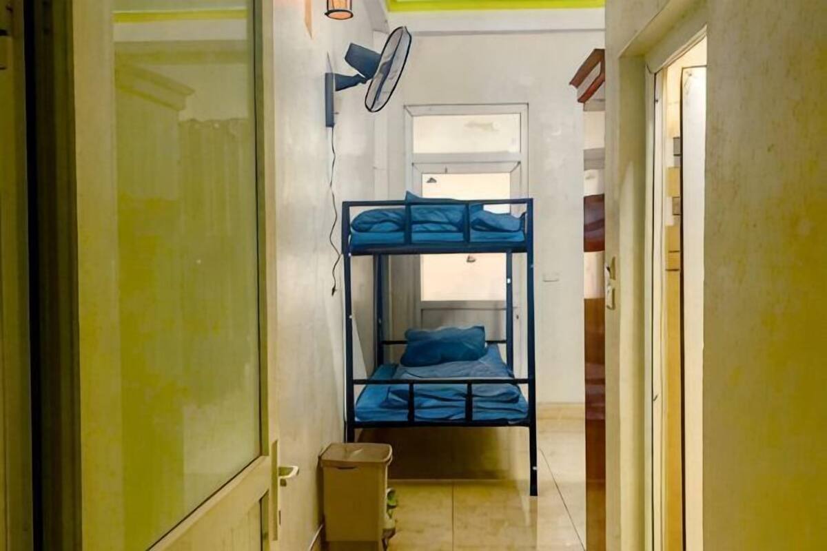 A narrow hallway with bunk beds, a fan, and a door leading to another room.