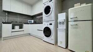 A modern kitchen with white cabinets, a double washing machine, a white refrigerator, and a microwave. - EunhasuD&M Residence Hotel (Daejeon)