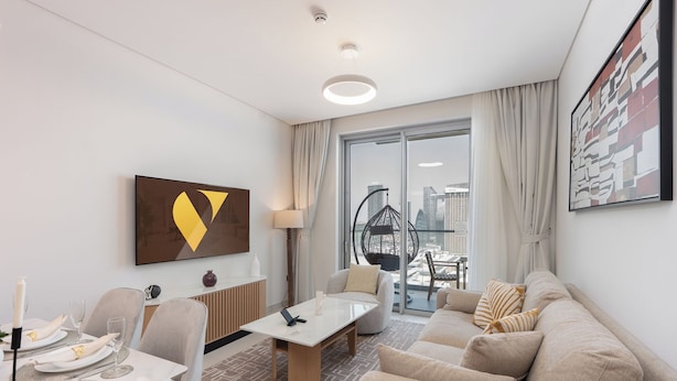 A modern hotel room with a dining area, a sofa, a hanging chair, and a city view through large windows.