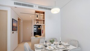 A modern dining area with a table set for four, a kitchen in the background, and a framed picture on the wall.