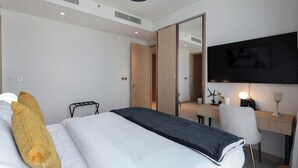 A modern hotel room with a bed, a desk, a chair, a TV, and a mirror.