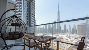 A balcony with a hanging chair, wooden table, and chairs, overlooking a cityscape with tall buildings.