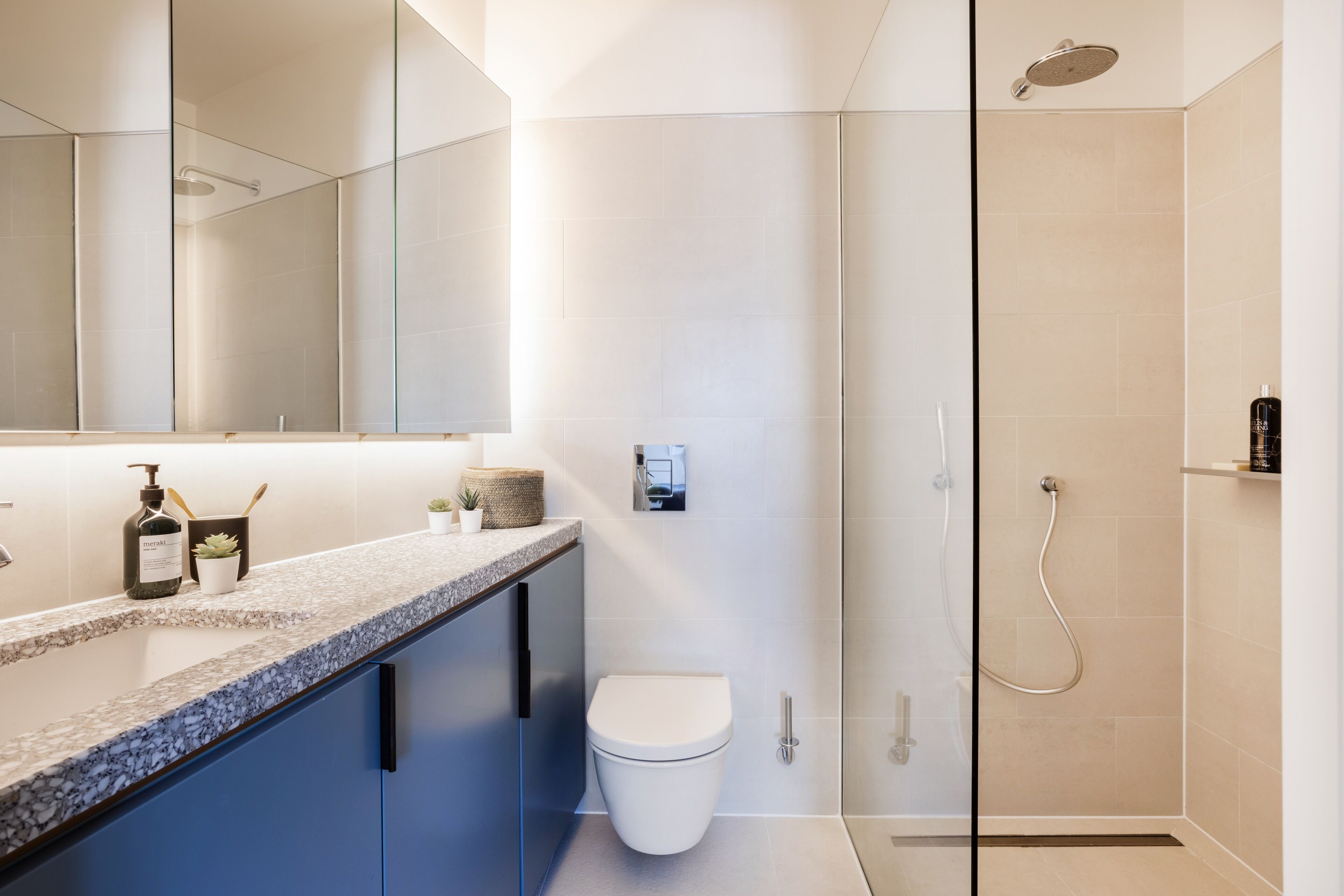 Un baño moderno con cabina de ducha de vidrio, inodoro blanco y encimera de mármol con artículos de aseo.
