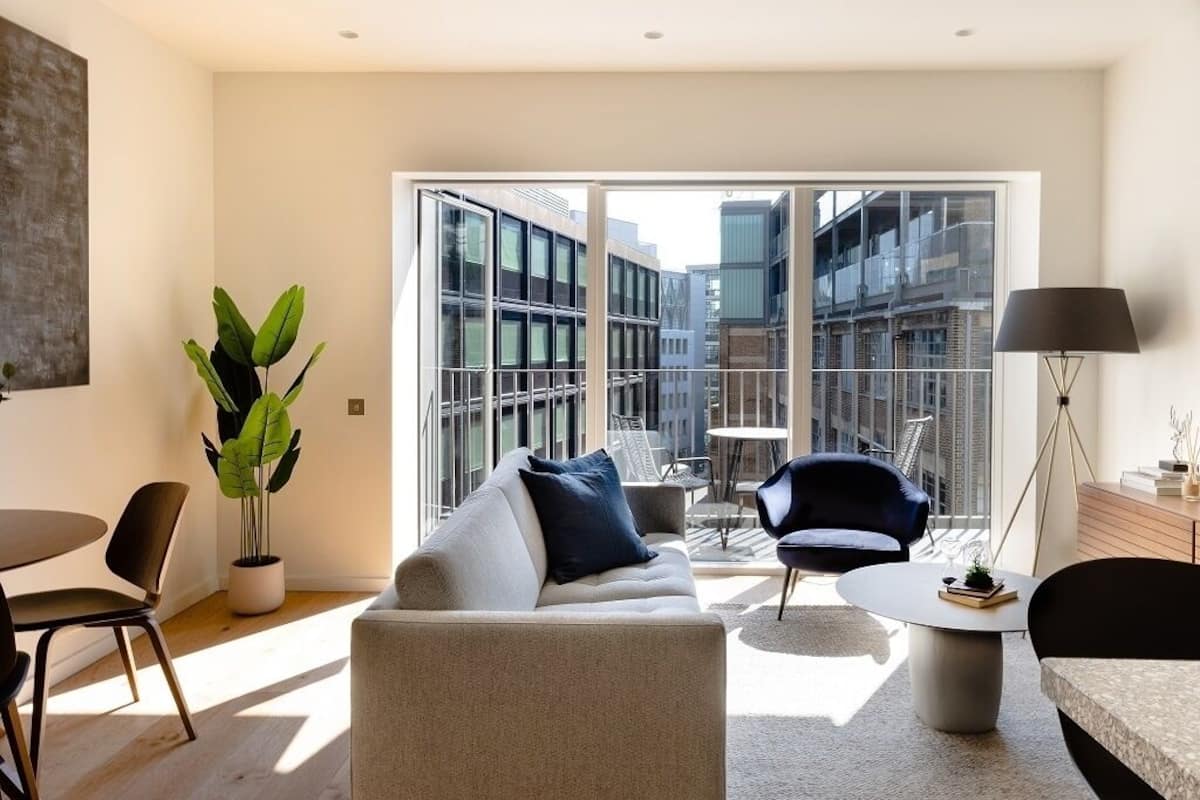 Un salon moderne comprenant un canapé, des fauteuils, une table basse et une grande fenêtre donnant sur le paysage urbain.