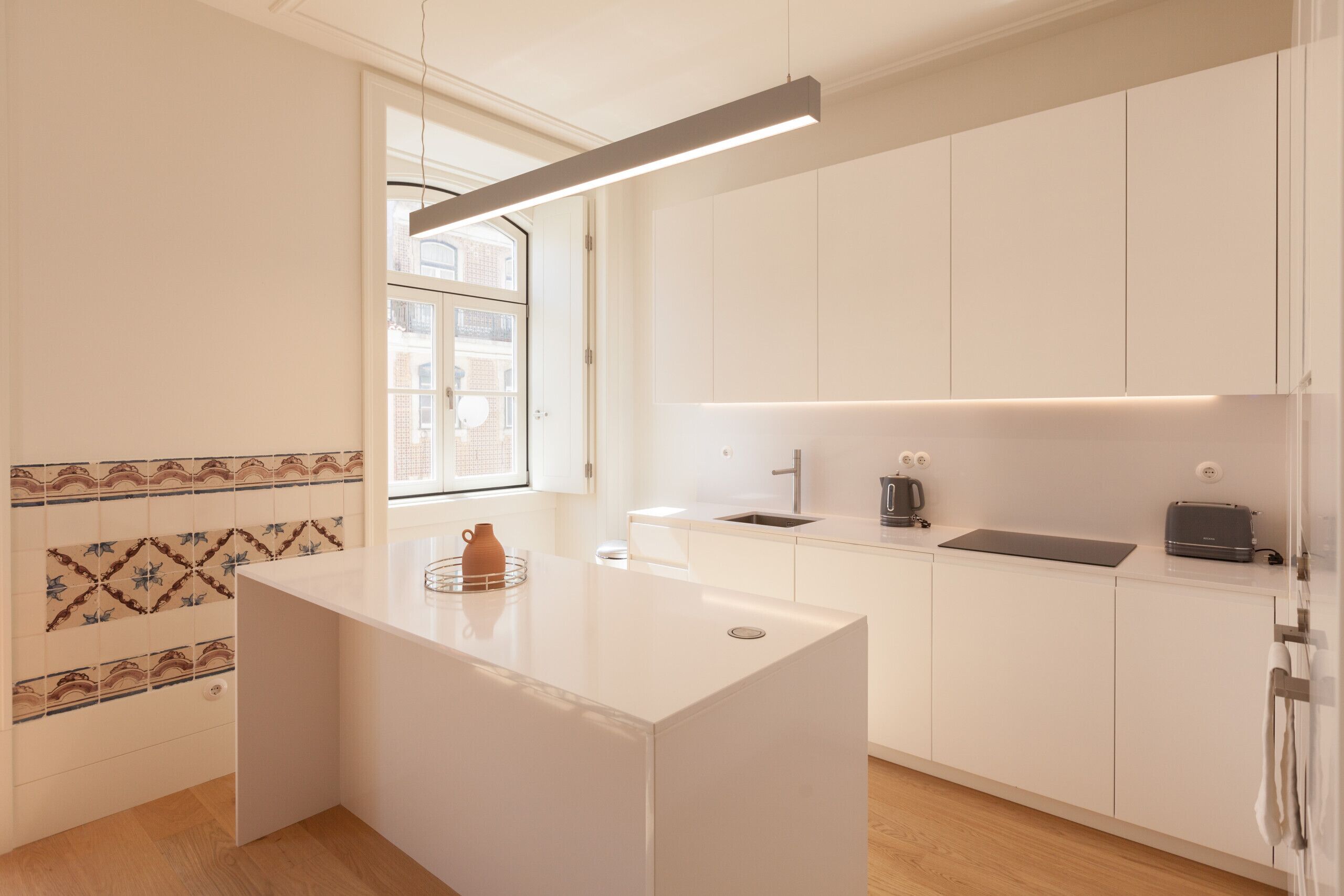 A modern kitchen with white cabinetry, a central island, a window, and a patterned backsplash.
