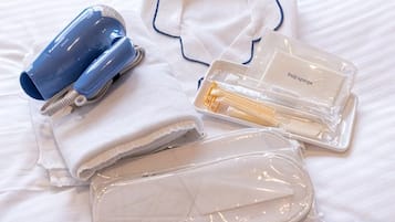 Ein ordentlich arrangiertes Set an Pflegeprodukten auf einem Bett, darunter ein Föhn, eine Lotionflasche und eine Kosmetiktasche.