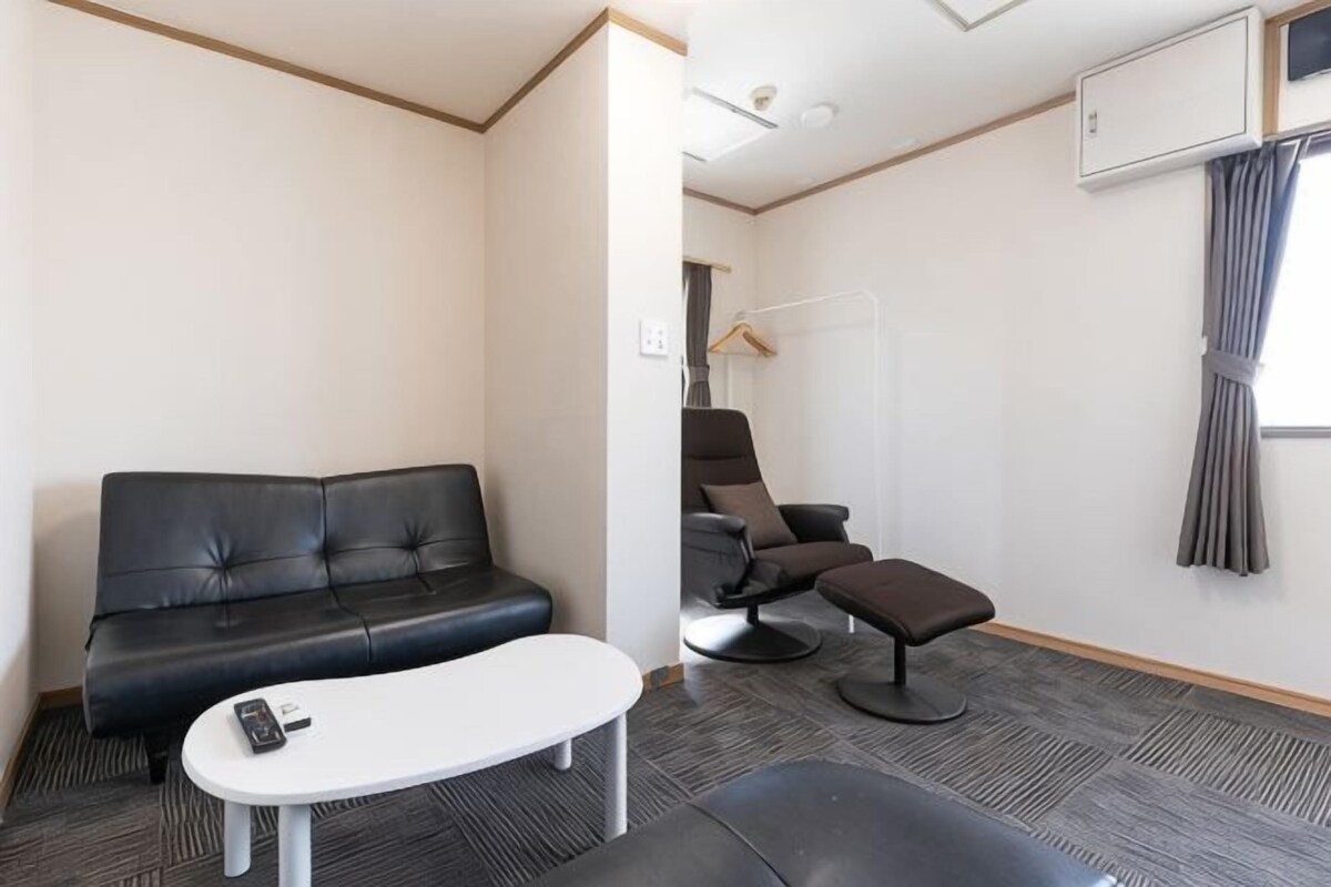 A room with a black leather sofa, a white table, a massage chair, and a small ottoman.