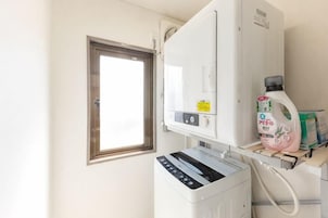 Una habitación funcional con ventana, lavadora y un estante pequeño con productos de limpieza.