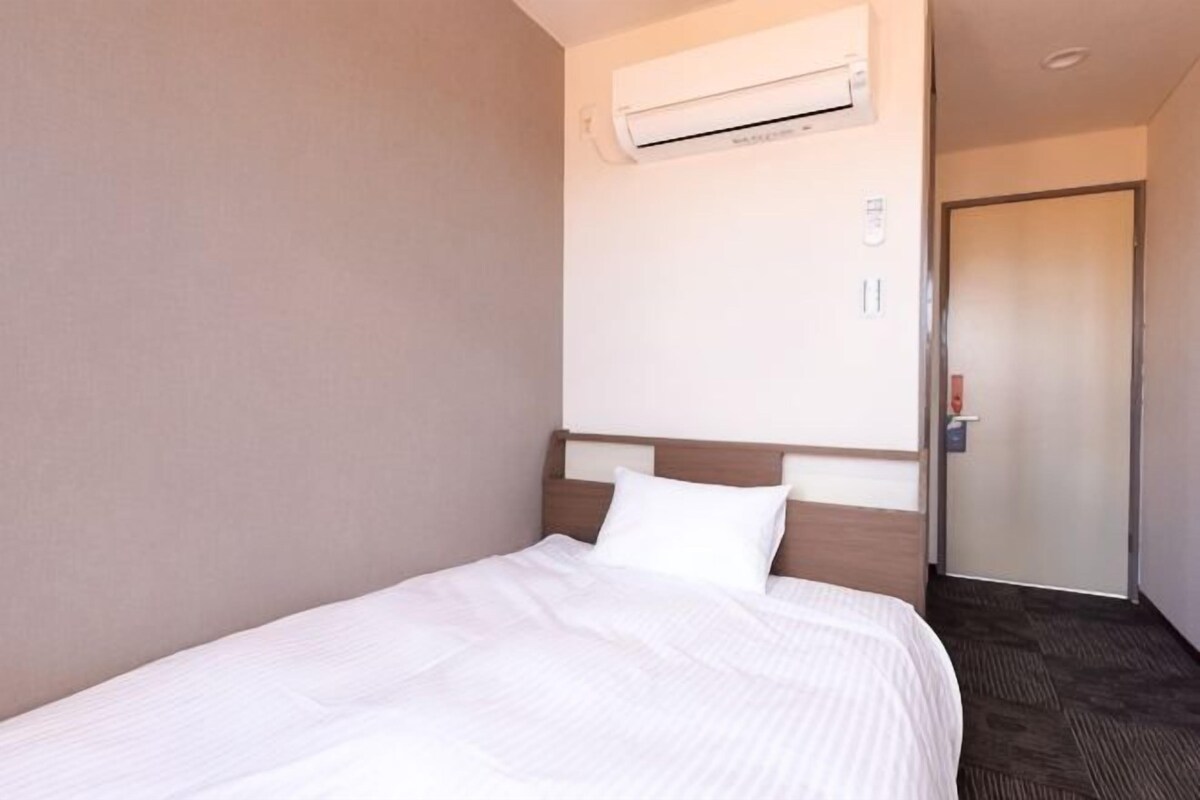 A hotel room with a bed, an air conditioning unit, a door, and a carpeted floor.