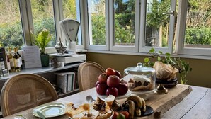 A dining table with various food items, a chair, a potted plant, and a window with a view of greenery. - Relaxation between vineyards and ocean, family house with swimming pool,Bordeaux (Plassac)