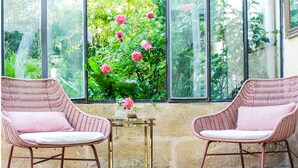 A conservatory with two wicker chairs, a small table, and a view of a garden through large windows. - Relaxation between vineyards and ocean, family house with swimming pool,Bordeaux (Plassac)