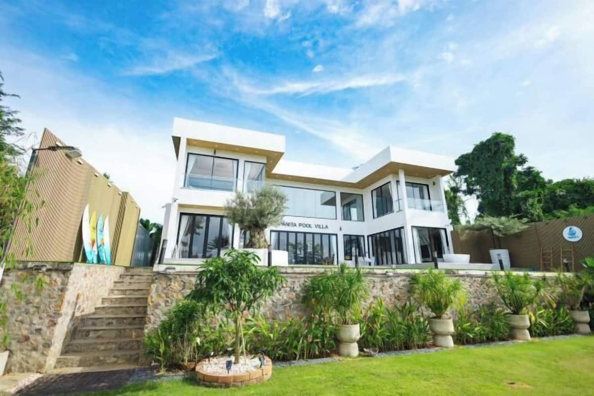 A modern villa with a stone staircase, a pool, and lush greenery.