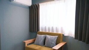 A room with a sofa, a window with curtains, a wall-mounted air conditioner, and a wooden floor. - Gracia Hotel (Osaka)