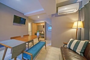 A dining area with a table and chairs, a sofa with a striped pillow, and an air conditioning unit on the wall. - Gracia Hotel (Osaka)