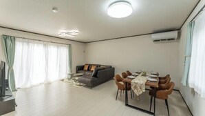 A modern living room with a sofa, dining table, and chairs, a flat-screen TV, and a ceiling light. - Yume Terrace at Yachimata (Yachimata)
