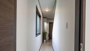 A narrow hallway with a wooden door on the left, a potted plant, and a light switch on the right. - Yume Terrace at Yachimata (Yachimata)