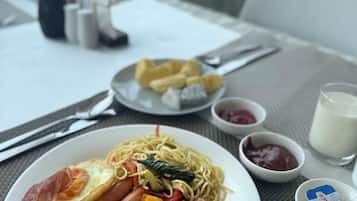 A meal with noodles, eggs, and sausages on a plate, accompanied by condiments and a glass of milk.