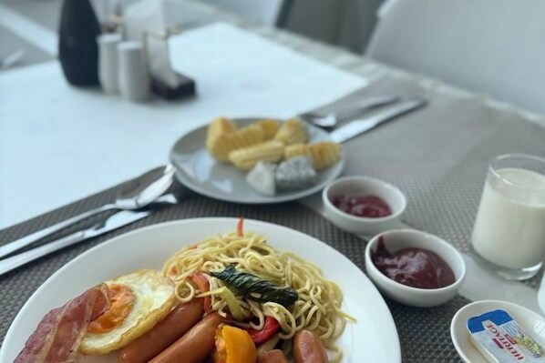 A meal with noodles, eggs, and sausages on a plate, accompanied by condiments and a glass of milk. - Twin Hotel Kampot (Kampot)