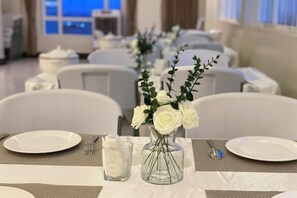 En festlokal med bord uppdukade för ett formellt evenemang, med vita dukar, glas och blomsterarrangemang som dekoration.