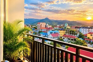 A balcony with a view of a town and mountains during sunset.