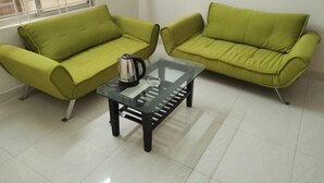A room with two green sofas, a glass coffee table, and a kettle. - China Inn Ltd (Dhaka)