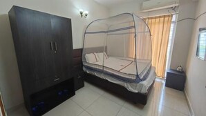 A bedroom with a bed under a mosquito net, a wardrobe, and a window with curtains. - China Inn Ltd (Dhaka)