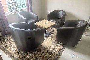 A room with a patterned rug, a small square table, and four black leather chairs arranged around it.