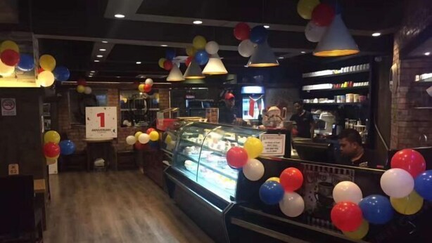 A restaurant interior with a glass display case, balloons, and a sign indicating a 1st anniversary. - China Inn Ltd (Dhaka)