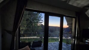 A room with a large sliding glass door leading to an outdoor patio with a chair and a table. - ZEN Luxury Houses & Spa Zlatibor (Municipality of Cajetina)