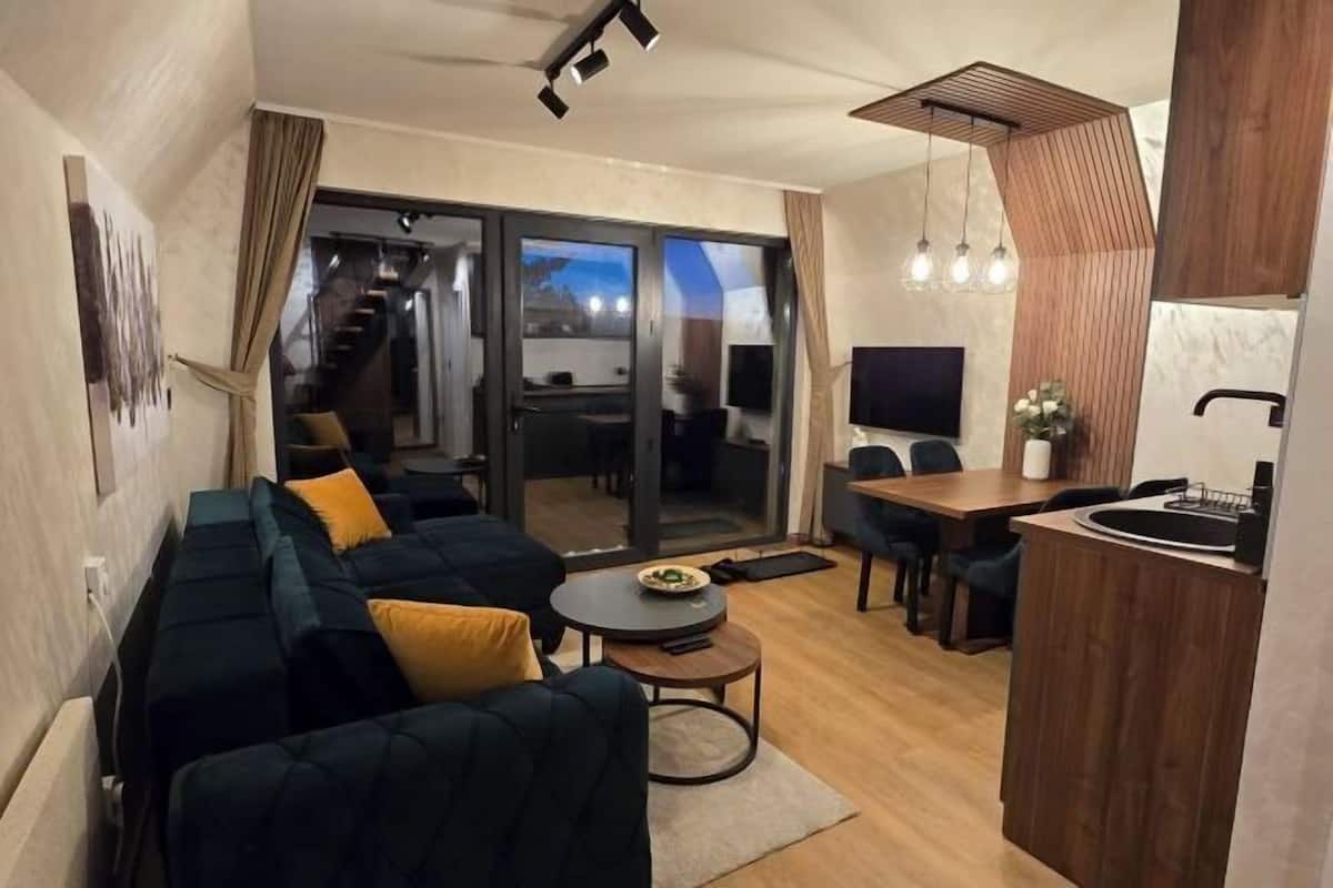 Un salon moderne avec un canapé, une table à manger et un téléviseur. Un escalier mène à un balcon.
