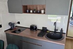 Una kitchenette compacta con tostadora, hervidor, pileta y un pequeño estante con tazas y una planta.