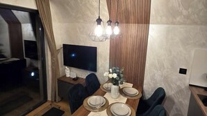 A dining area with a wooden table, chairs, a TV, and a decorative vase. - ZEN Luxury Houses & Spa Zlatibor (Municipality of Cajetina)