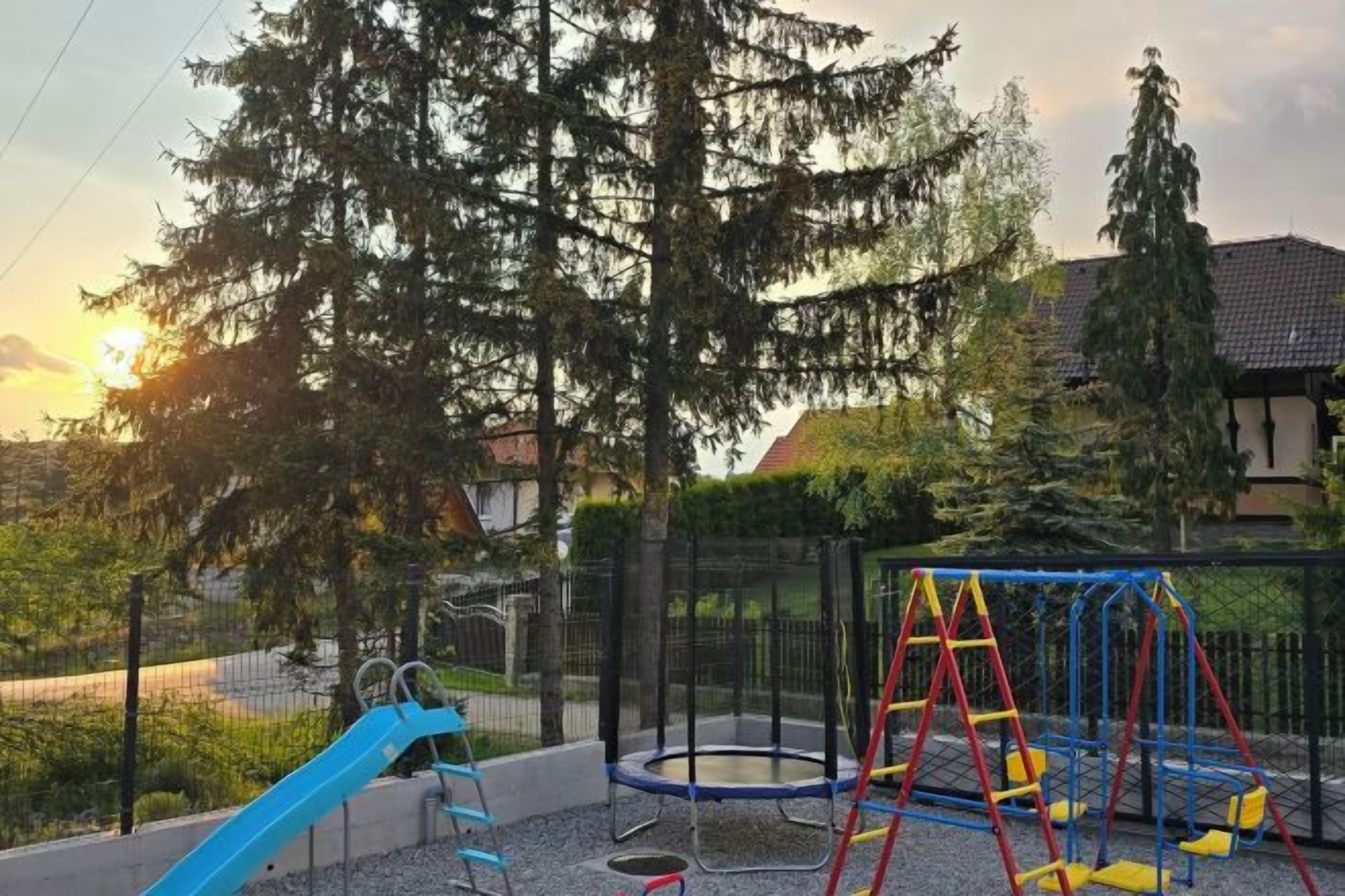 A playground with a slide, swing set, and trampoline.