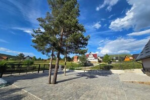 Un espacio exterior empedrado con un árbol, una cerca y casas al fondo.