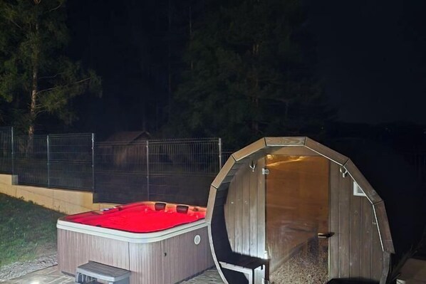 Un jacuzzi y una estructura de madera, posiblemente una sauna o baño de vapor, al aire libre de noche.