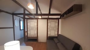 Ein Zimmer mit Holzboden, einem grauen Sofa, einem weißen Tisch und einer traditionellen japanischen Schiebetür.