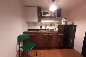 A compact kitchen with a microwave, sink, and a refrigerator. A green chair is placed near the counter. - [new] Hanok - Hyehwa 1937 (Seoul)