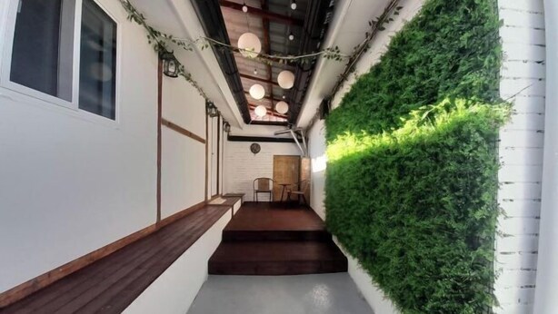 Ein schmaler Flur mit einer hölzernen Bank, einer vertikalen grünen Wand aus Pflanzen und einer Treppe, die zu einer oberen Ebene führt.