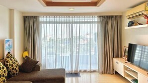Una sala de estar con sofá, televisor y cortinas.