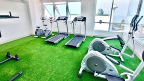 Un gimnasio con cintas de correr, bicicletas estáticas y máquinas elípticas sobre césped artificial.