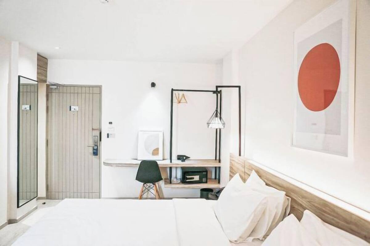 A modern hotel room with a bed, desk, chair, and a large wall art piece.
