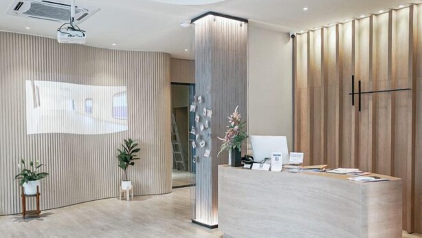 A modern reception area with a curved reception desk, vertical wooden paneling, and potted plants.