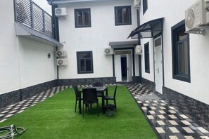 A courtyard with a table and chairs, surrounded by a white building with black trim and air conditioning units.