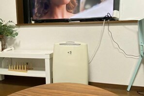 A room with a television mounted on the wall, a white cabinet with a plant, and a white device on the floor. - Garfield Home Shinjuku (Tokyo)