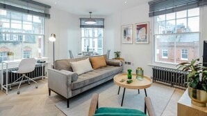 A modern living room with a grey sofa, a round coffee table, and a dining area with a white chair and table. - Kula London - Fitzrovia Newman St (London)